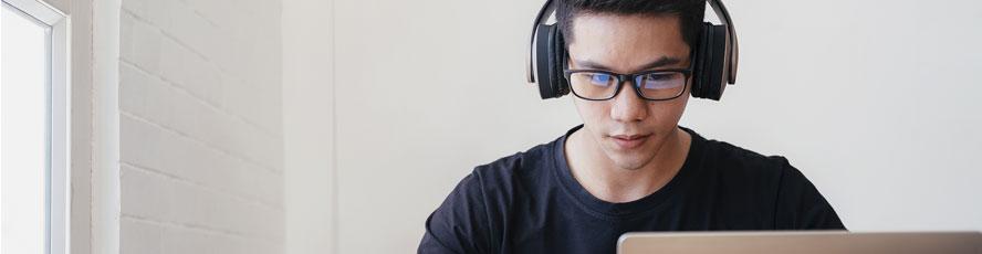 Photo of a student behind a laptop wearing headphones