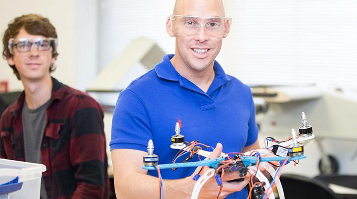 一名澳门赌场航空课程讲师手持一架小型无人机，一名学生在一旁观看